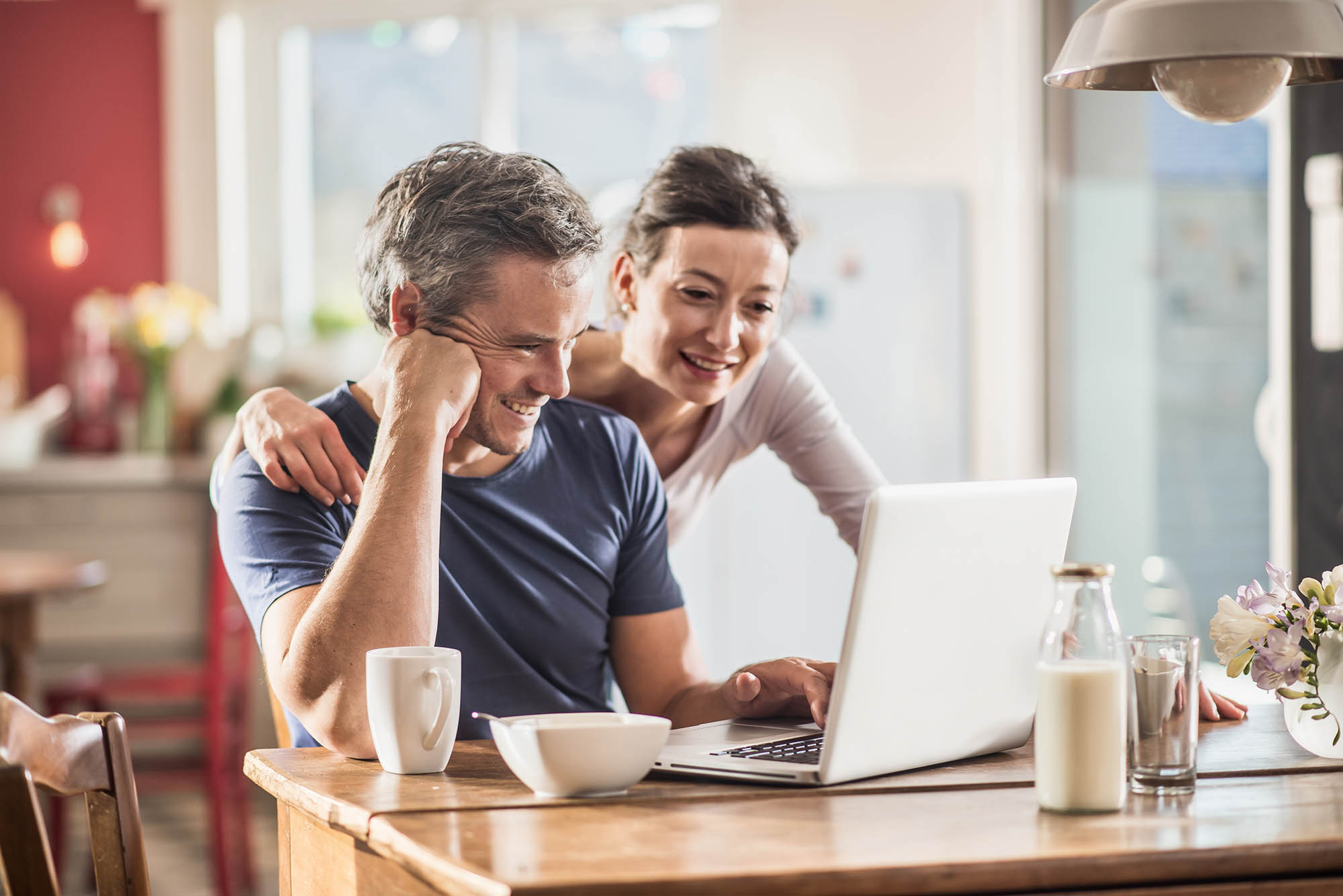 A Couple Using A Laptop While Having Breakfast In The Kitchen